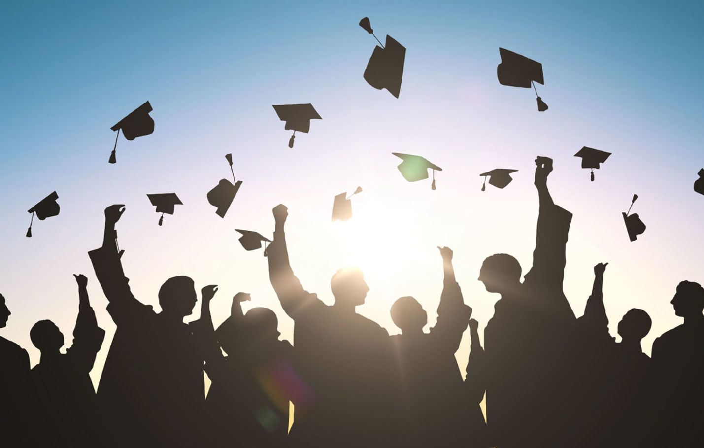 Graduating students dressed in robes throw their caps into the air