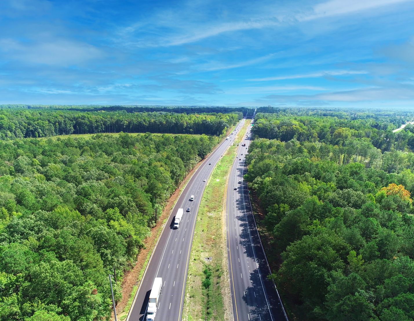 Cars driving on six lanes of traffic with a grassy median separting them