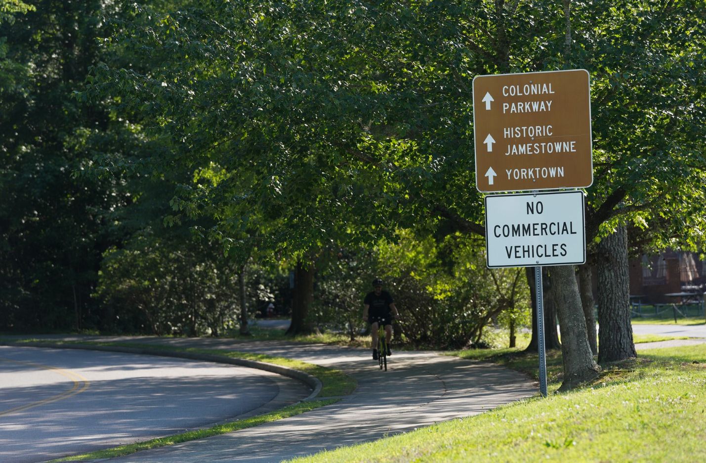 A cyclist rides past two signs, one of which directs people to the Colonial Parkway, Historic Jamestowne, and Yorktown