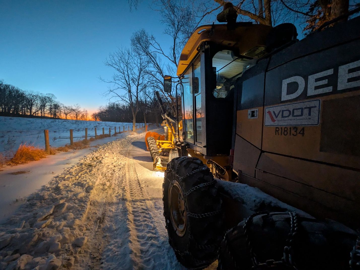 A VDOT grader plows snow on a rural road.