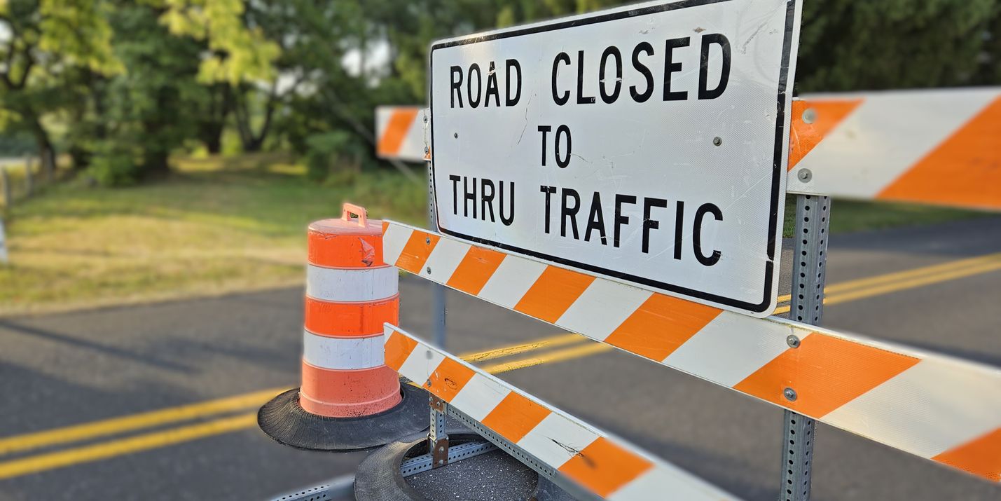 Road Closed sign on an orange and white barrier with a blurred background of trees