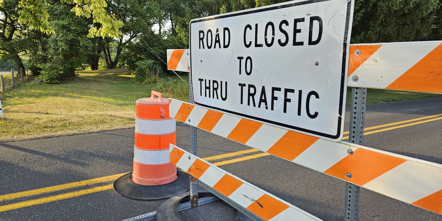 Road Closed sign on an orange and white barrier with a blurred background of trees