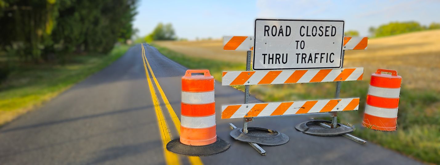 Road Closed sign on an orange and white barrier with a blurred background of a two-lane roadway