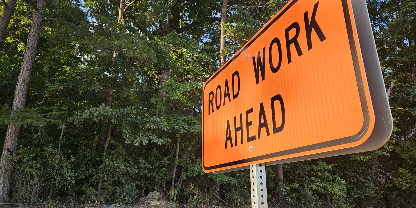 Road Work Ahead sign at a sharp angle with trees in the background