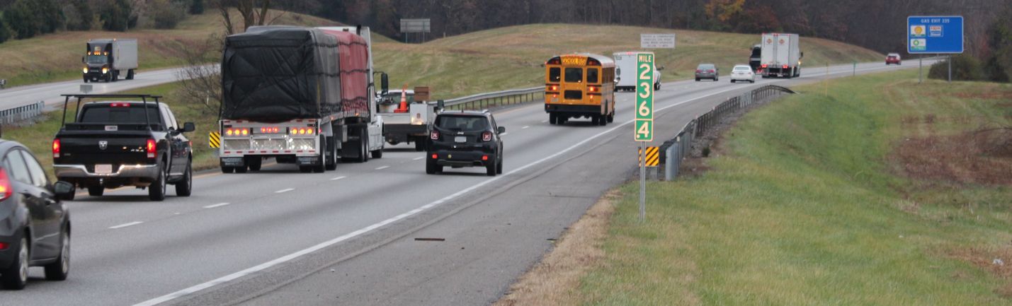 Interstate traffic including trucks and school bus driving up a long grade on an overcast day