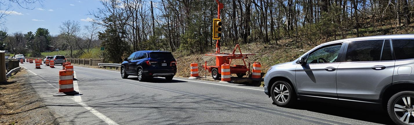 Vehicles moving along a two-lane road and bridge, with a portable signal controlling traffic.