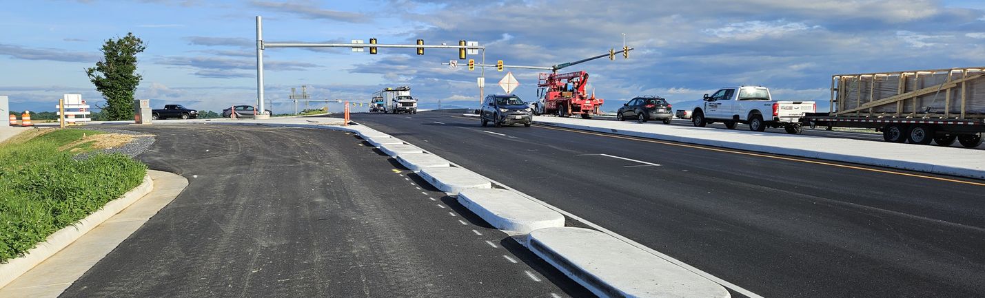 Sunny day photo of a signalized intersection of two multi-lane roadways. Moderate traffic and under-construction areas are visible.