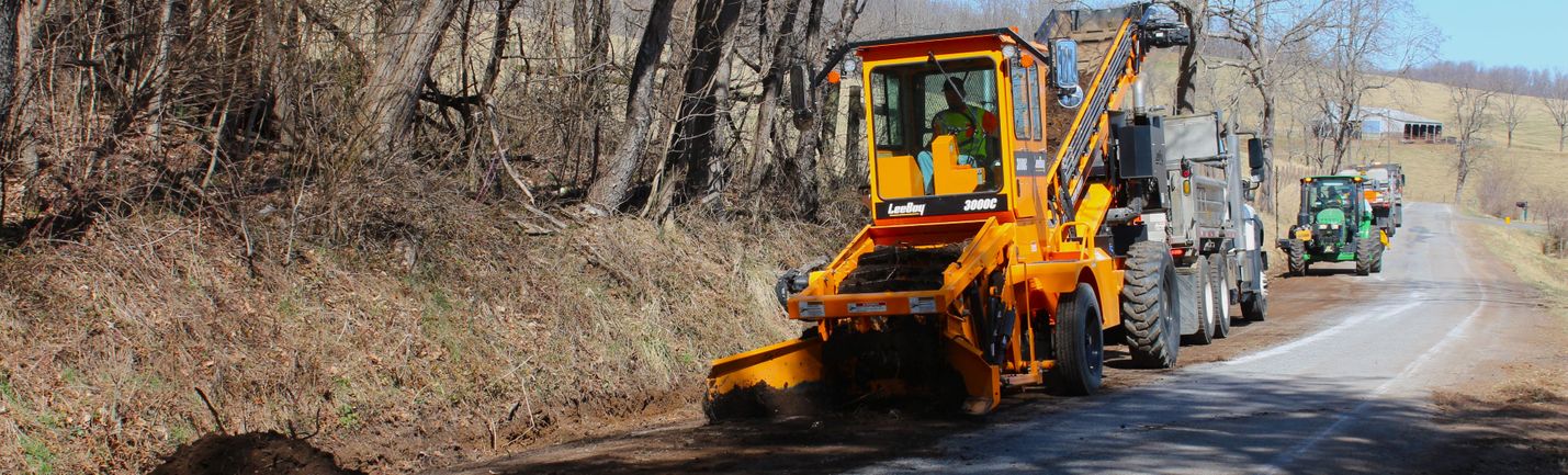 Heavy equipment improving drainage ditch along a two-lane road in a rural area