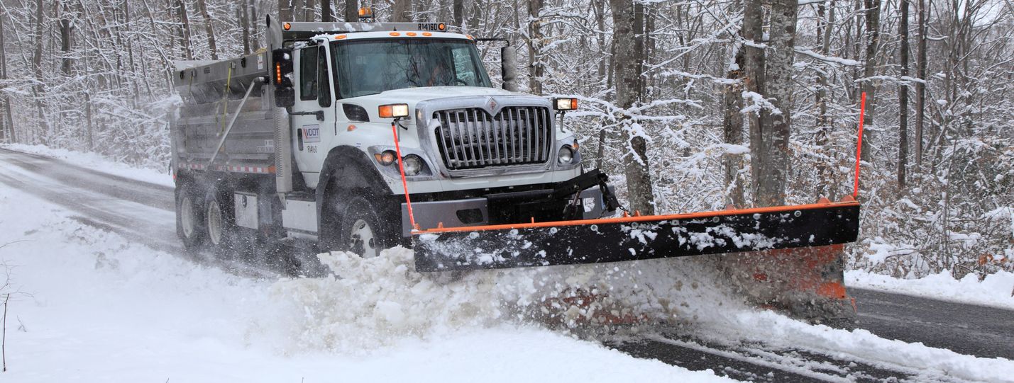 VDOT snowplow working along a rural road with trees in the background