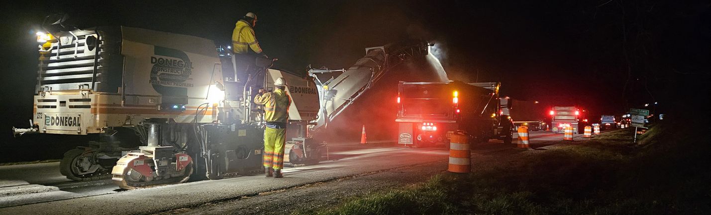 Nighttime photo of construction workers and heavy equipment working along a highway