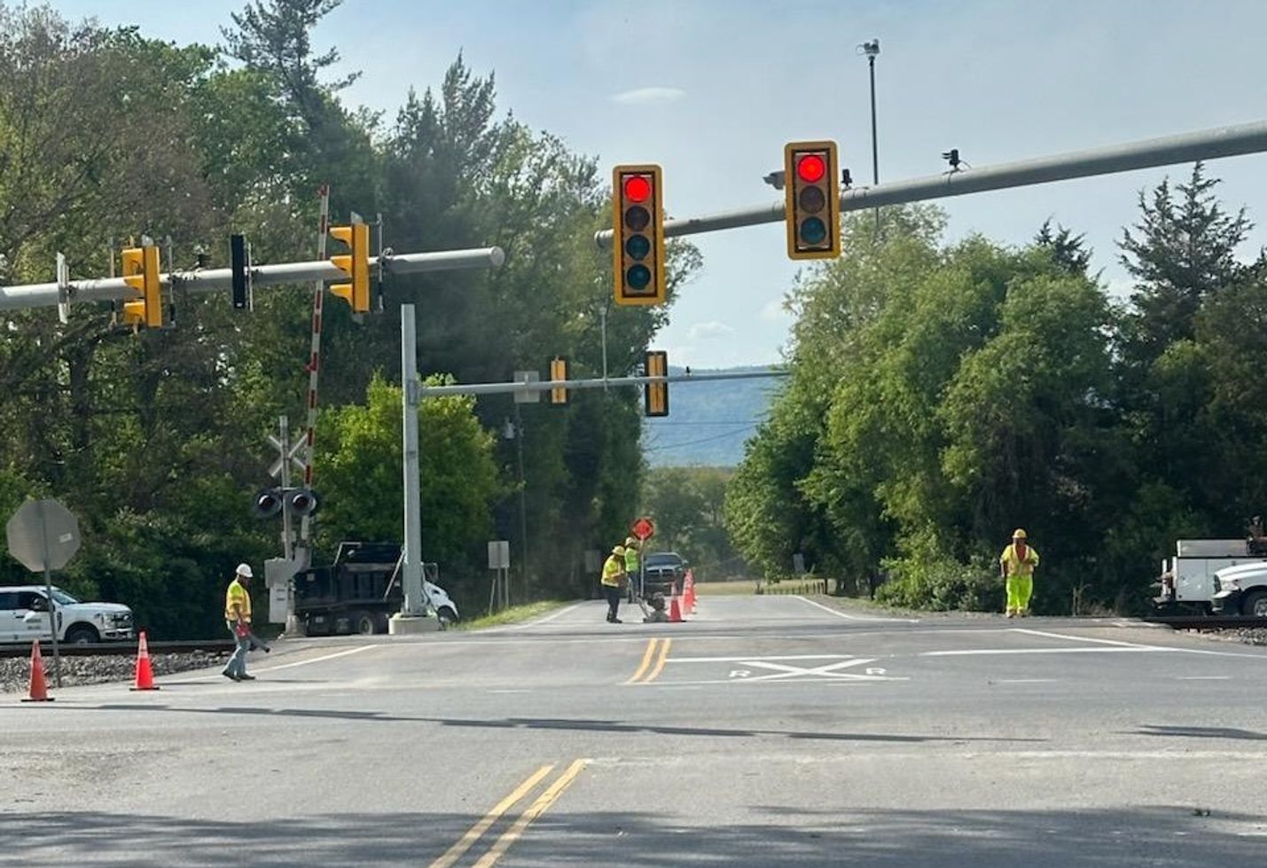 Construction crews and equipment around a traffic signal at a rural roadway intersection.