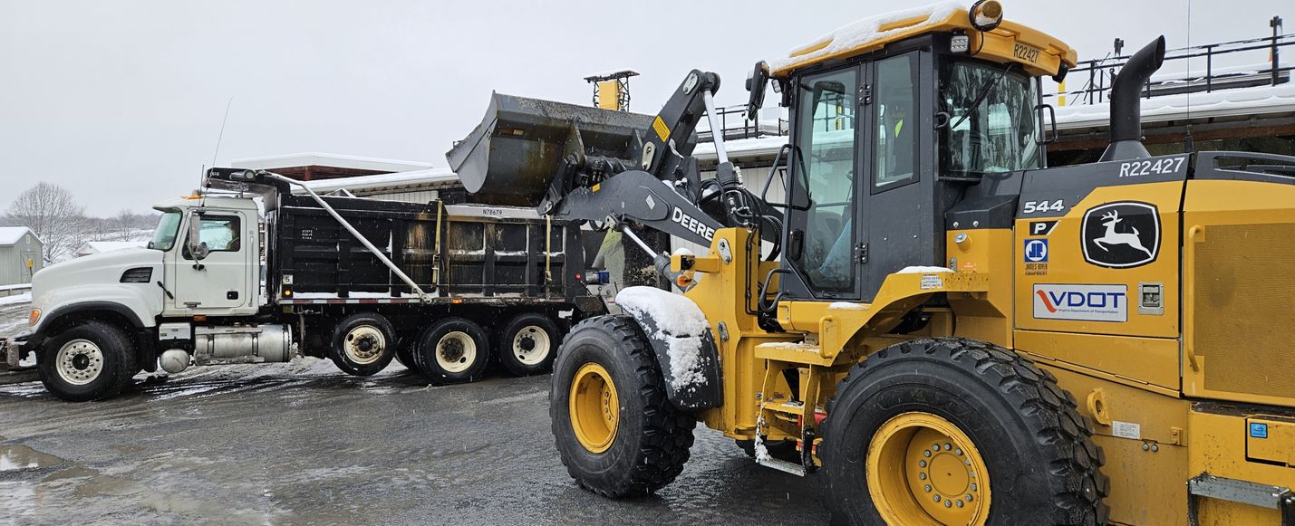 Photo of front-end loader filling a snowplow's hopper with road salt