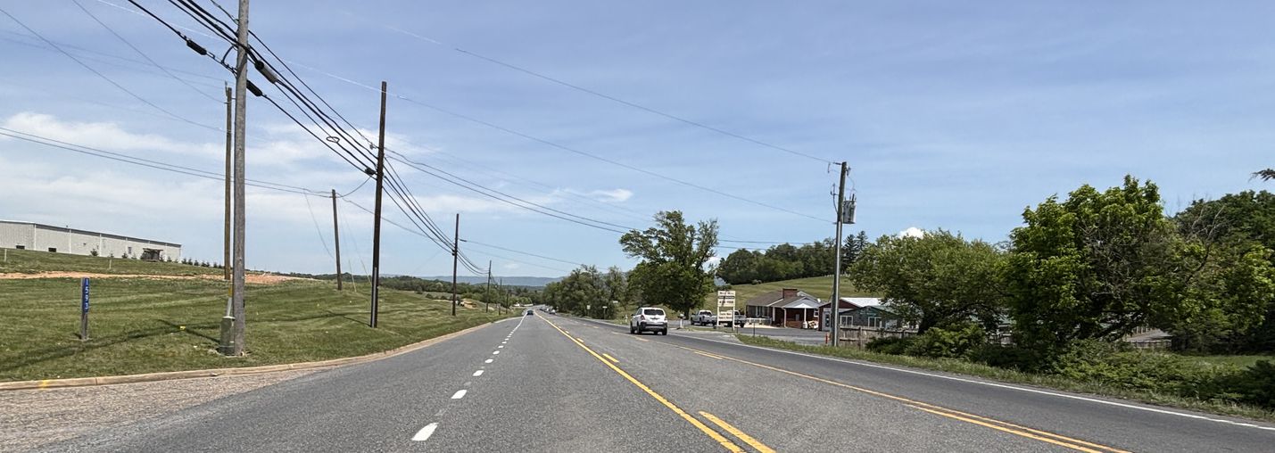 Photo of a five-lane roadway with light traffic under a clear sky with buildings and trees in the background