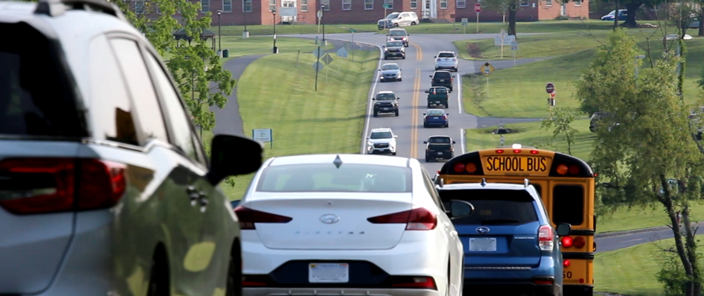 Photo of traffic congestion on a two-lane roadway extending into the distance. An intersection is in the background, and grassy areas line the roadway.