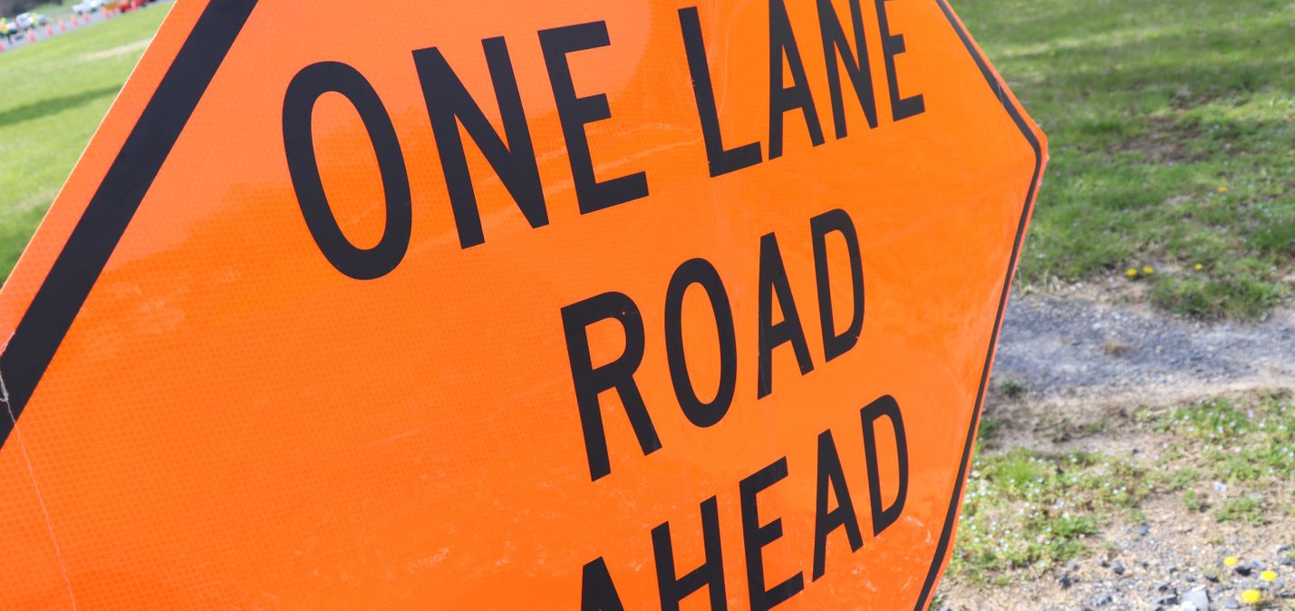 Orange traffic sign viewed at a sharp angle, with the words ONE LANE ROAD AHEAD