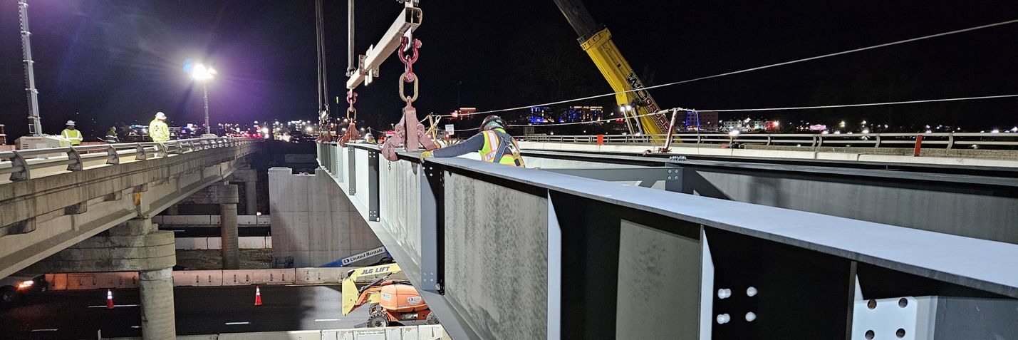 Nighttime photo of crews placing steel beams for new bridge