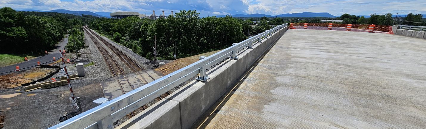 Photo taken from the edge of a nearly completed bridge, looking down on railroad tracks and an at-grade crossing