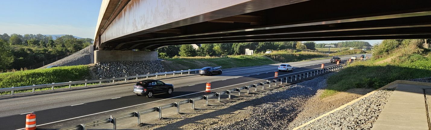 Moderate traffic on a multi-lane highway, passing under a bridge on a sunny morning.