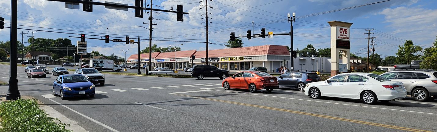 Traffic on a five-lane roadway at a signalized intersection. Blue cloudy skies and commercial businesses are in the background.