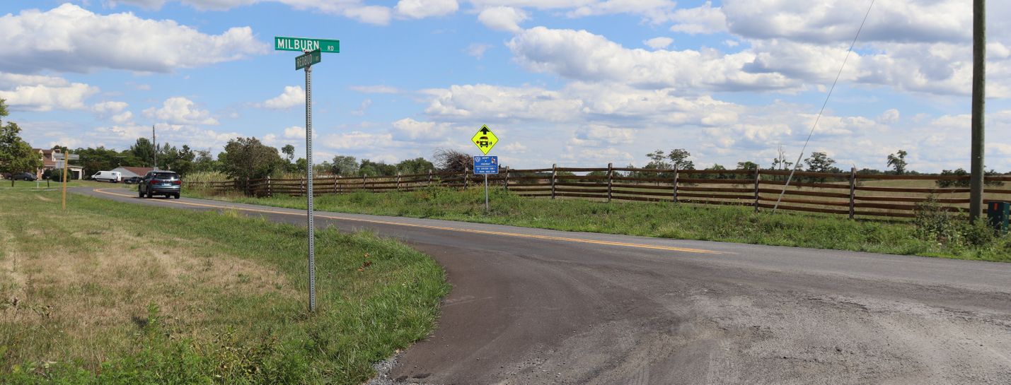 Intersection of two secondary roads on a sunny day. A sport-utility vehicle is visible in the distance on one of the roads.