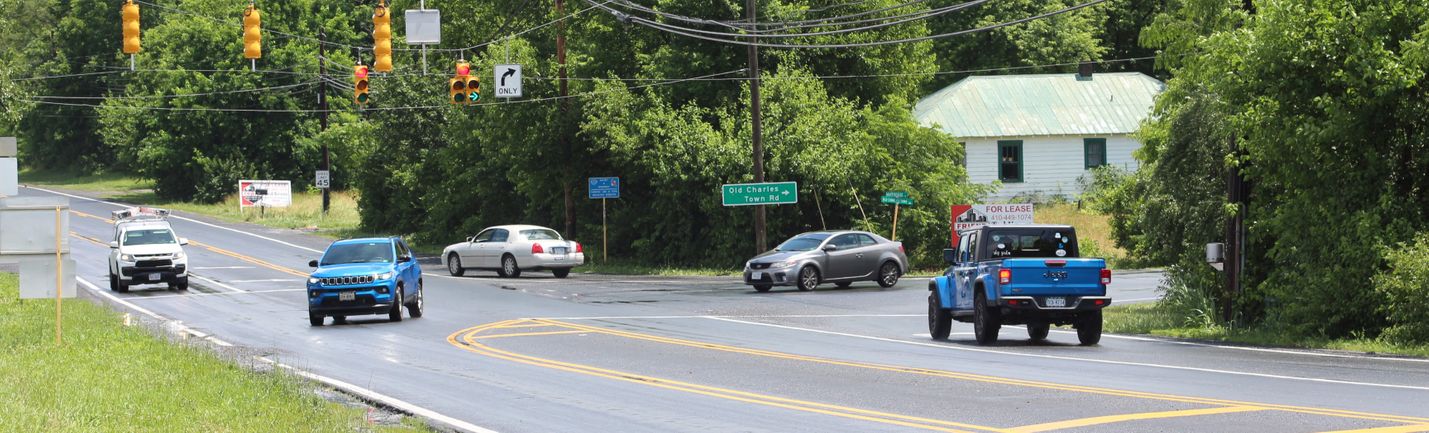 Signalized intersection of a pair of two-lane roads, showing moderate traffic on a rainy summer day
