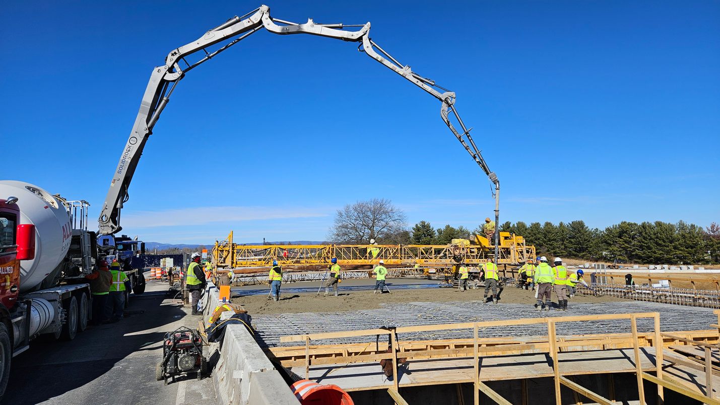 Construction crews pouring concrete for a new bridge over a highway on a clear winter day