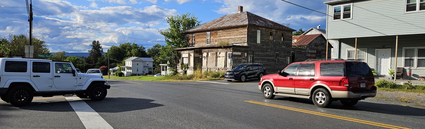 Traffic approaching the intersection of a pair of two-lane roads on a mostly sunny day. The intersection is flanked by commercial and residential buildings.