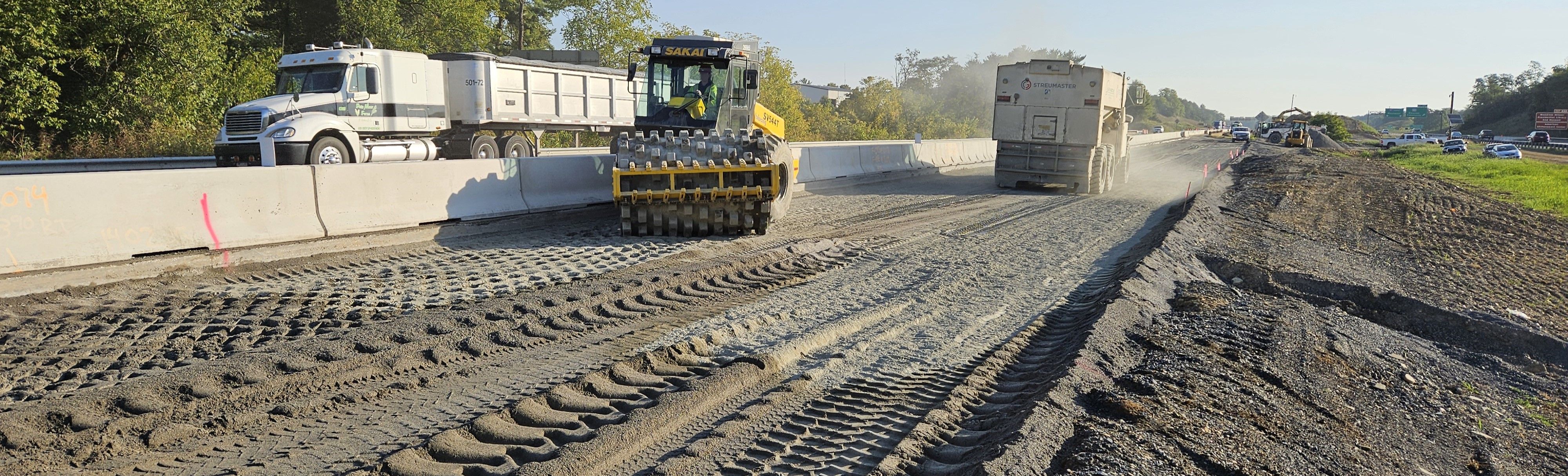 Heavy equipment spreading material in the media between two interstate lanes as traffic drives by