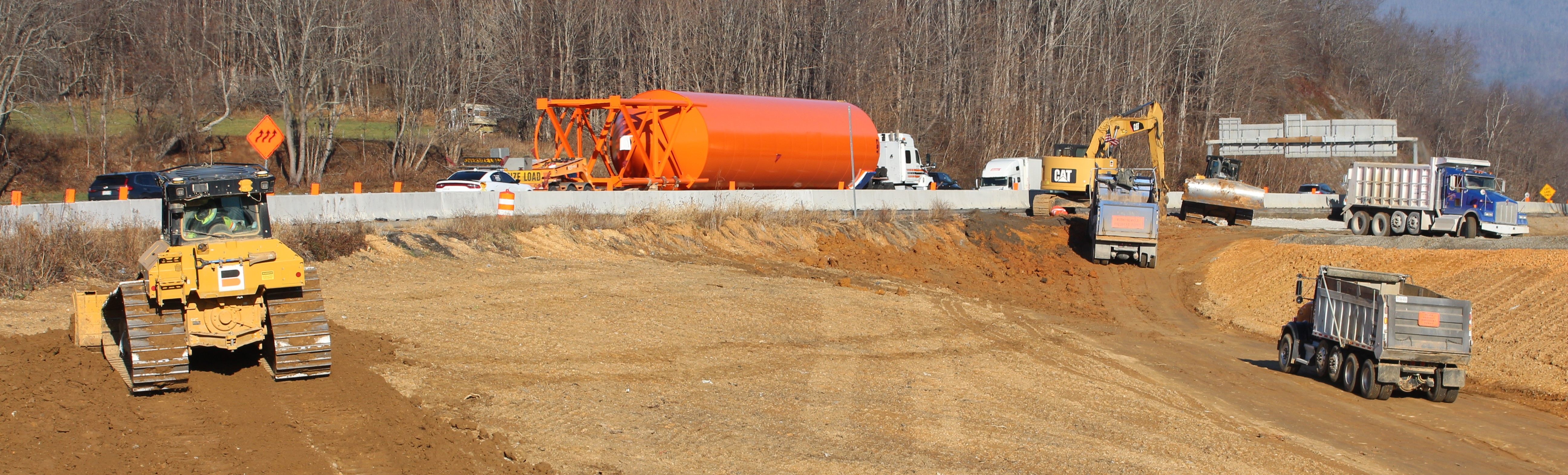 Earth-moving operations with heavy equipment in the foreground and highway traffic in the background.