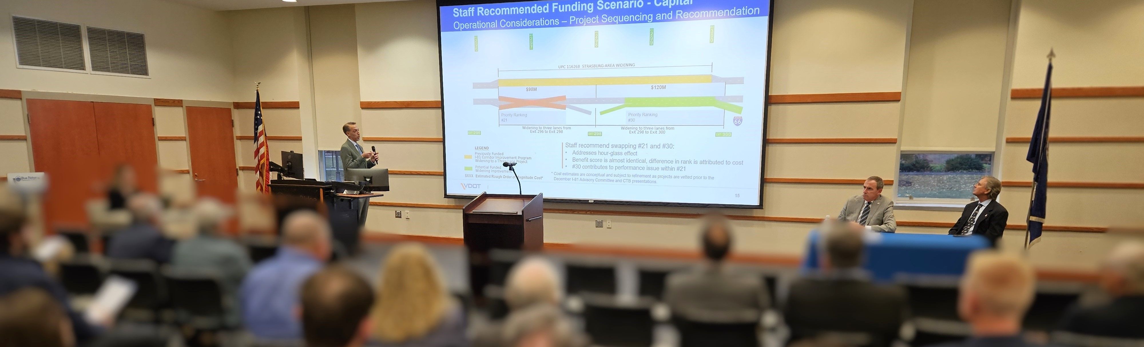 A roomful of people looking at a presentation with text and graphics on a shared computer screen