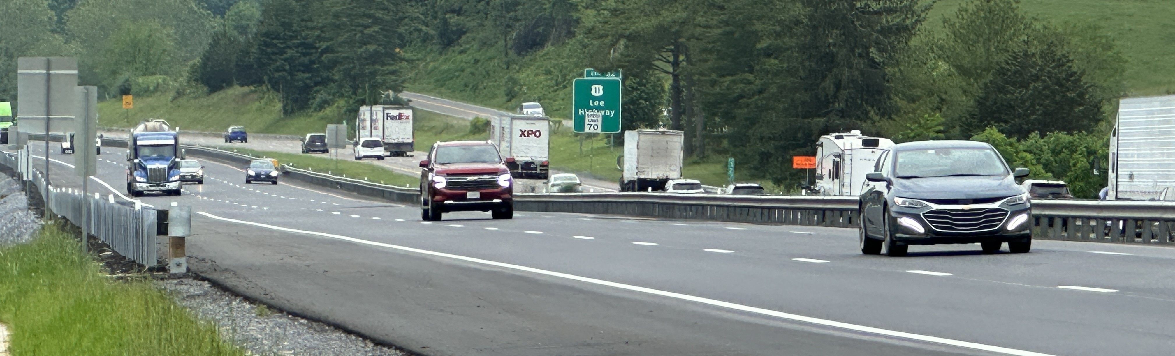 Photo showing three lanes of highway traffic driving up a steady uphill grade in a rural area during an overcast spring day