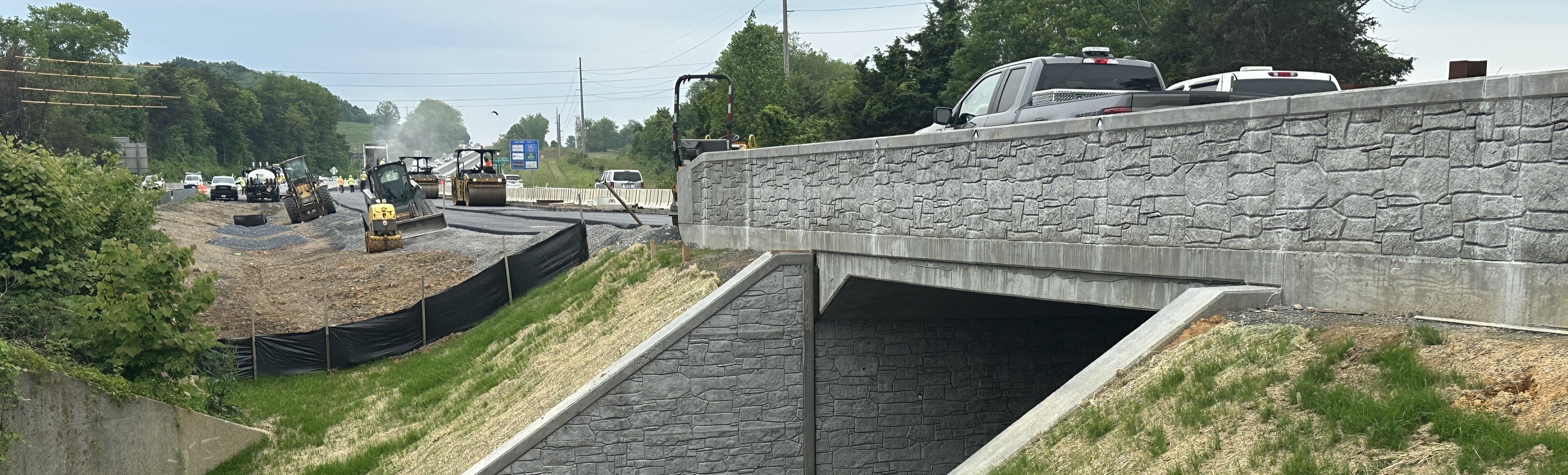 A low-angle photo showing a new bridge and paving work along a four-lane highway.