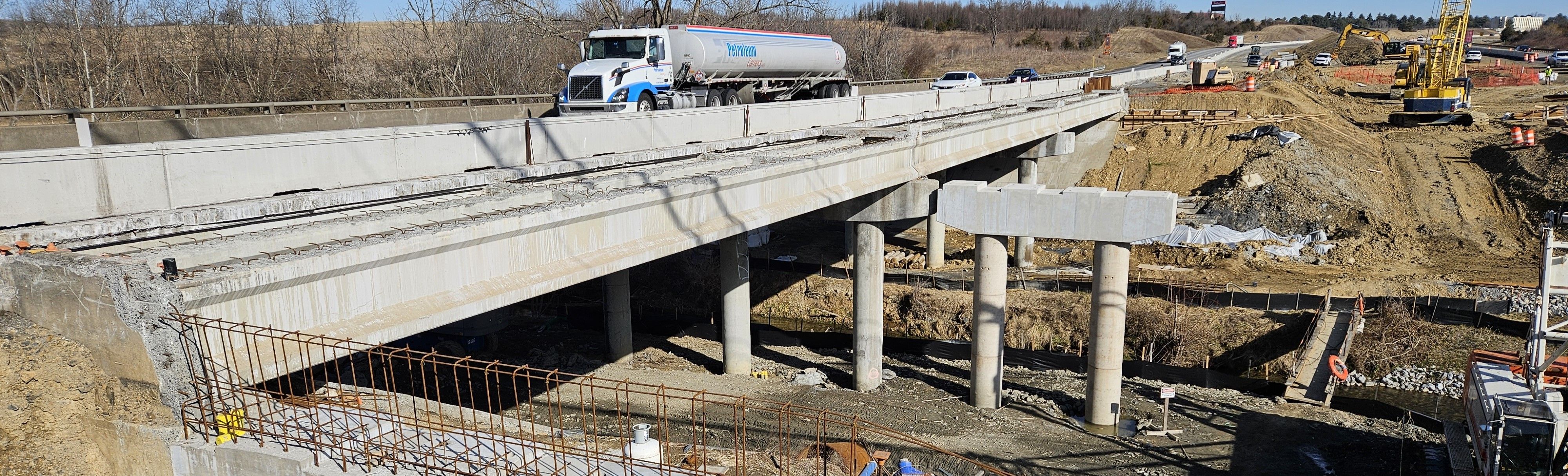 Traffic moving along an interstate bridge. A work zone is on the right, including bridge piers and abutments under construction.