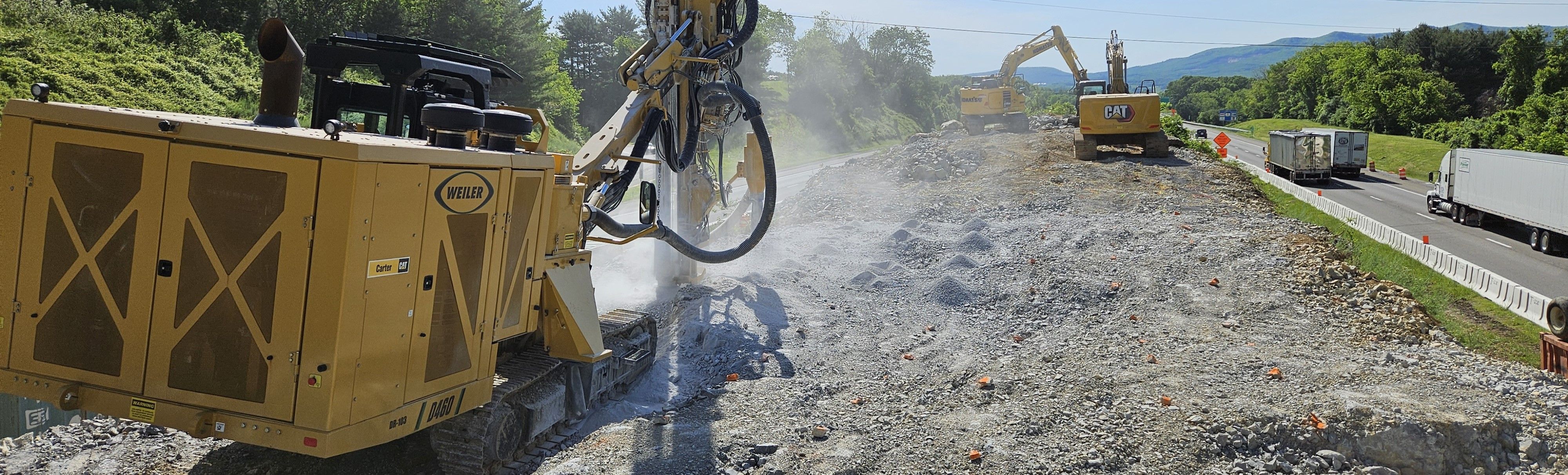 An industrial jackhammer and other heavy equipment in the median of a multi-lane highway. Light vehicular traffic is visible to the far right.
