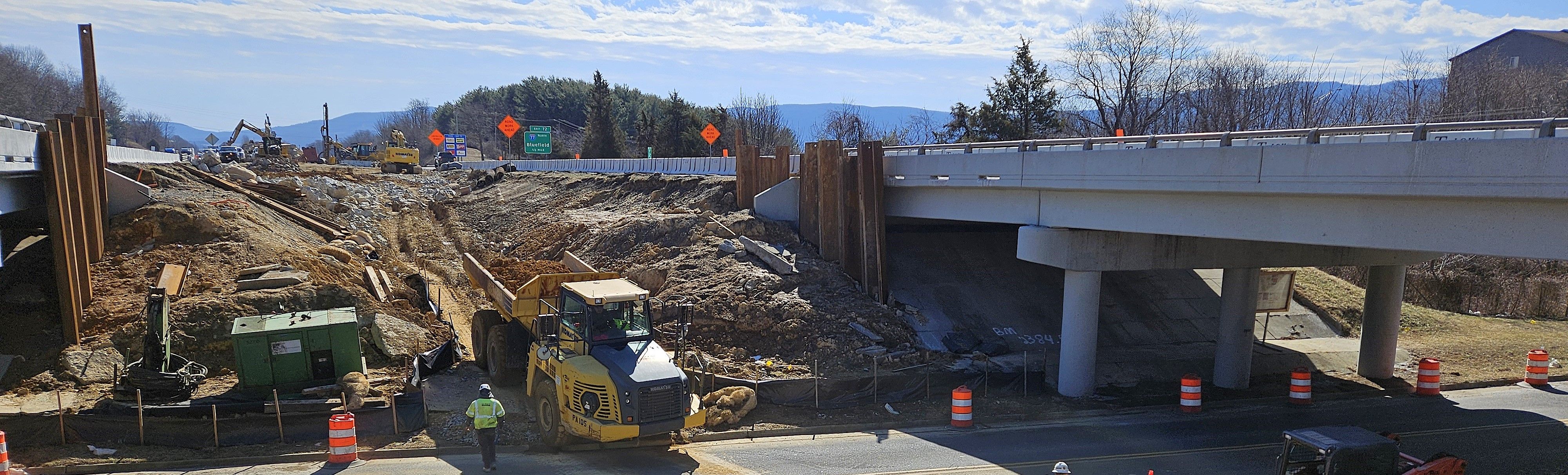 An industrial-sized dump truck moving between interstate travel lanes, down a slope between two bridges.