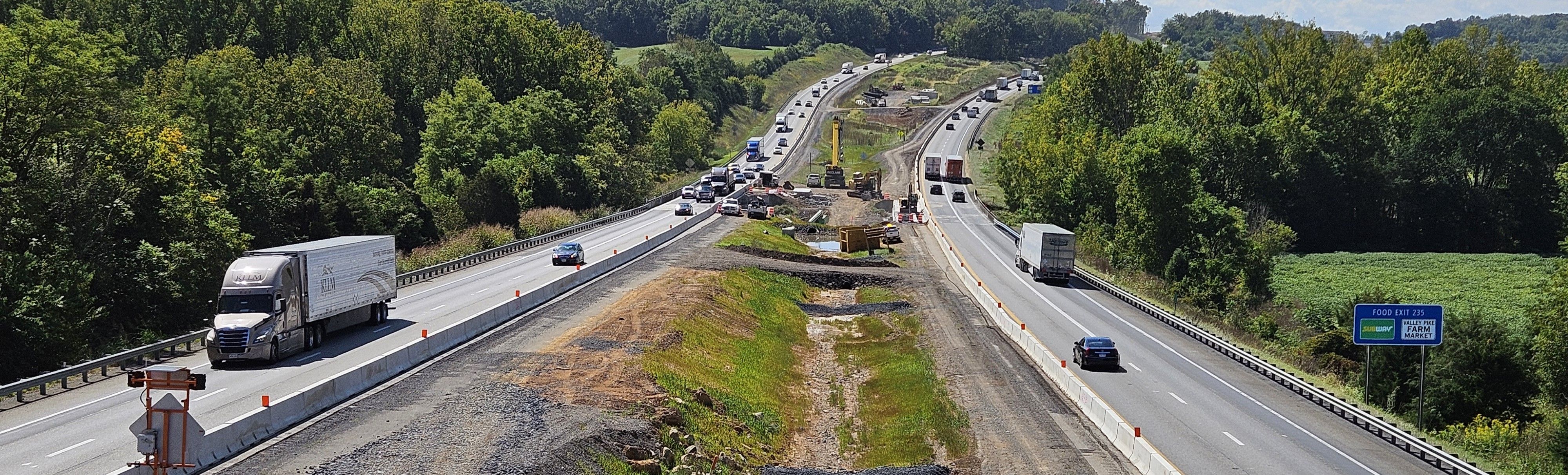 Elevated view of a four-lane divided highway with moderate traffic. Construction work and equipment are in the median.